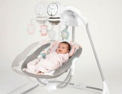 Happy newborn baby relaxing in a gentle side-to-side baby swing with soft padding and hanging toys for engagement