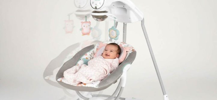 Happy newborn baby relaxing in a gentle side-to-side baby swing with soft padding and hanging toys for engagement