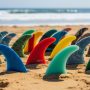 Collection of colorful recycled surfboard fins made from ocean plastic waste arranged on sandy beach