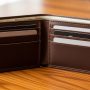 A premium full-grain leather bifold wallet in dark brown placed on a wooden surface, open to show card slots and cash compartment