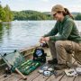 A beginner angler organizing basic fishing equipment including a rod, reel, tackle box, and line spooler on a wooden dock