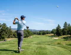 Mid handicap golfer hitting a driver on a fairway with a high launch golf ball in flight against a clear sky