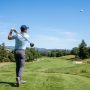 Mid handicap golfer hitting a driver on a fairway with a high launch golf ball in flight against a clear sky