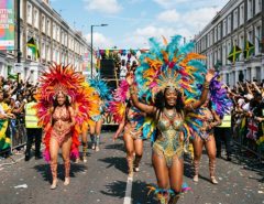 Colourfully costumed masqueraders parading down Ladbroke Grove with feathered headdresses and sequined costumes at Notting Hill Carnival 2026 in West London