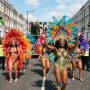 Colourfully costumed masqueraders parading down Ladbroke Grove with feathered headdresses and sequined costumes at Notting Hill Carnival 2026 in West London