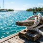 White marine rope secured tightly to a wooden dock cleat over blue water.
