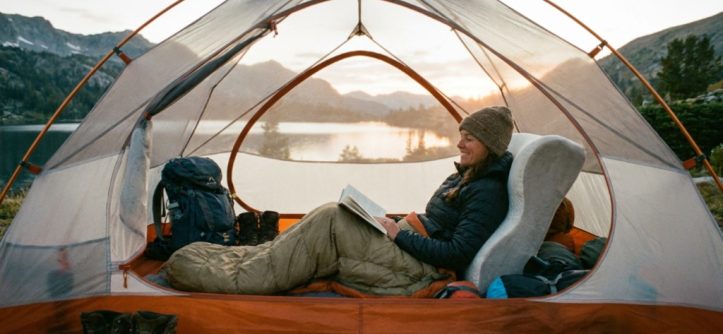 Compact memory foam camping pillow beside a hiking backpack on a wooden table.