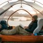 Compact memory foam camping pillow beside a hiking backpack on a wooden table.